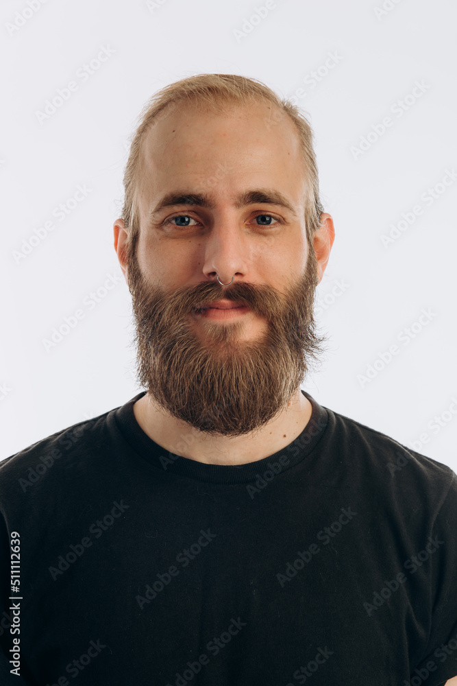 Fototapeta premium portrait of a young guy with a beard in a black T-shirt on a white background. hipster