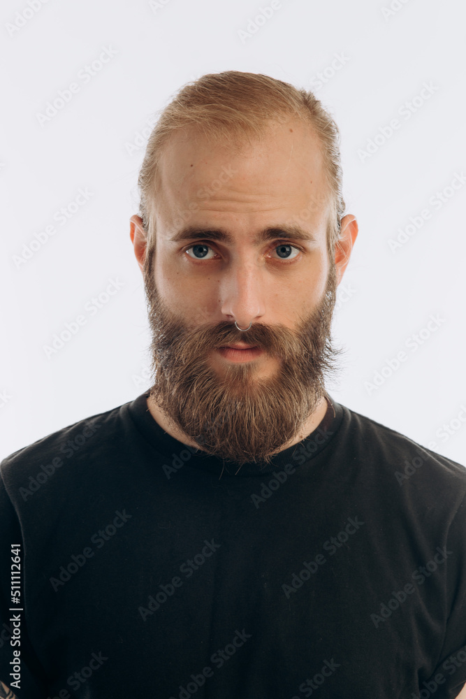 Obraz premium portrait of a young guy with a beard in a black T-shirt on a white background. hipster