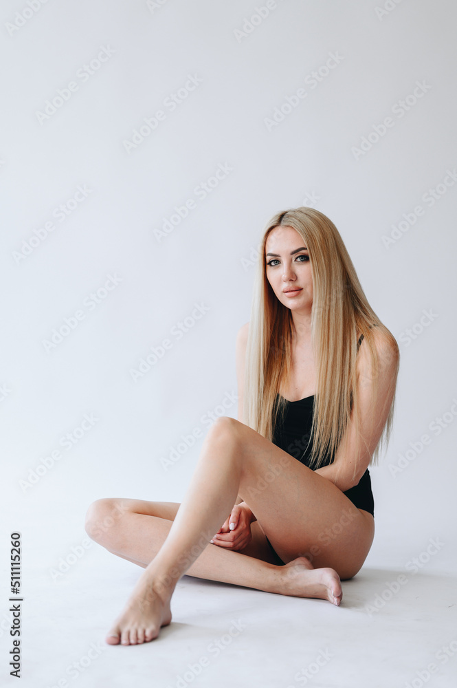 The girl is sitting on a white background in one bodysuit. Girl with a cute smile for foot care advertising The girl is sitting on a white background in one bodysuit. Girl with a cute smile for foot care advertising