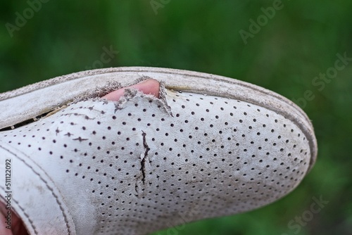 finger in a hole in one white old leather shoe on a green background