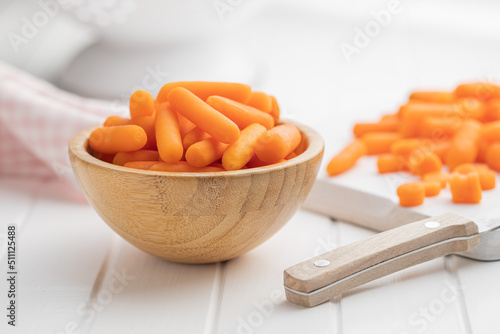Baby carrot vegetable in bowl. Mini orange carrots on white table. photo