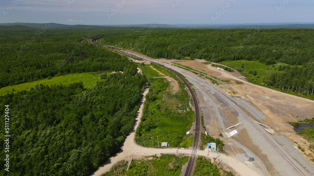 Aerial View of the Cargo Long Train in taiga, mountains near to dirt road with tracks