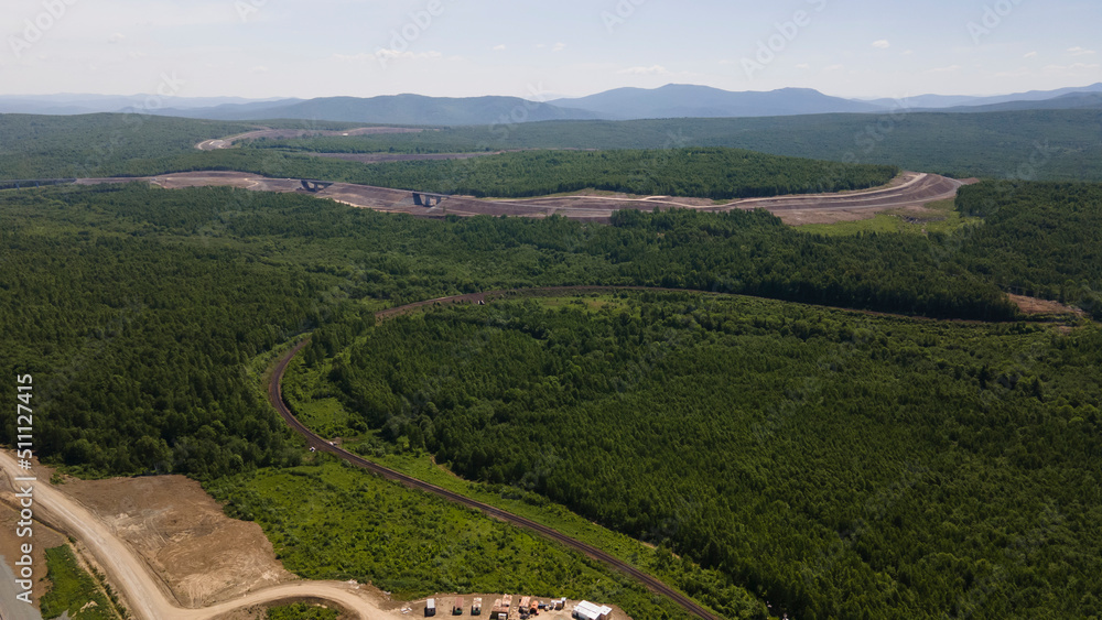 Aerial View of the Cargo Long Train in taiga, mountains near to dirt road with tracks in summer afternoon