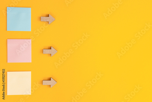 Colorful sticky notes and different wooden arrows on yellow background.