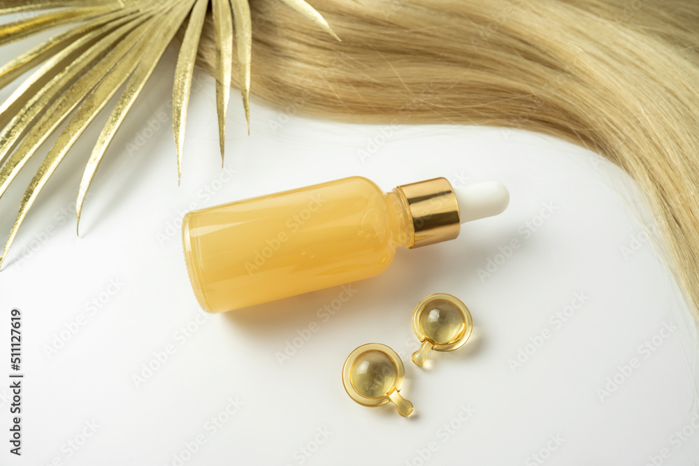 A natural oil or serum for hair care and golden treatment capsules lying on a white background