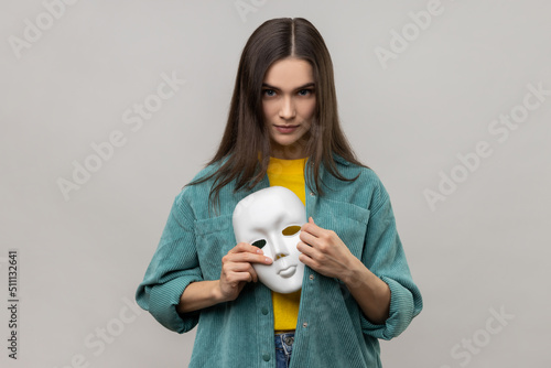 Canvastavla Portrait of serious bossy woman holding white mask in her hand, changing personality, hiding mask in the bosom, wearing casual style jacket