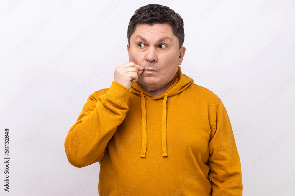 I won't tell anyone, promise. Middle aged man making zip gesture to close mouth, keeping secret, zipping lips, wearing urban style hoodie. Indoor studio shot isolated on white background.