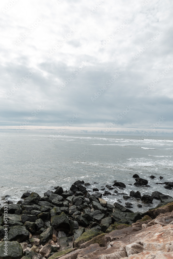 Beautiful sea view with water, stones, waves and a gray sky with clouds. Ocean scenery