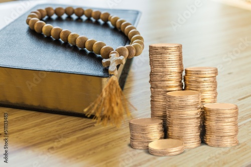 Fotografija A stack of coins with a Holy Bible Book in the background