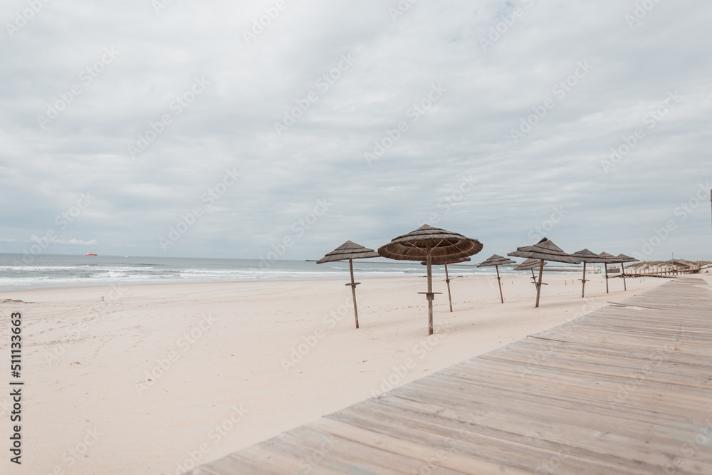 Empty sandy beach with a wooden walkway and straw umbrellas near the ocean. Vacation in Portugal. Atlantic Ocean. Vacation at sea.