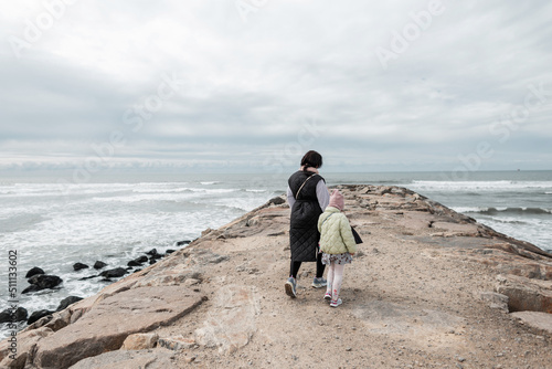Mother and daughter walking along a rock near the ocean. Family vacations by the sea in spring
