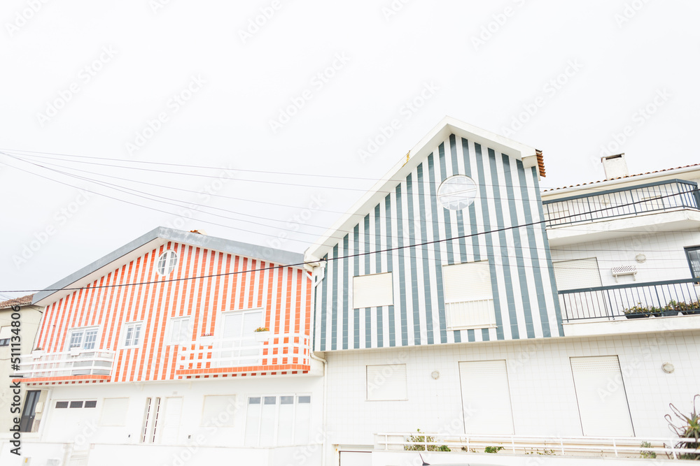 Obraz premium Beautiful vintage wooden striped house near a road with cars in Portugal. Beautiful fishing village with creative architecture. Vacation by the sea
