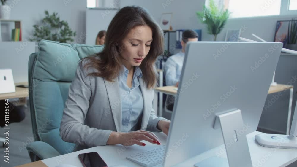 In modern office young businesswoman working typing on laptop computer. On background people working. Portrait. Close up In modern office young businesswoman working typing on laptop computer. On background people working. Portrait. Close up