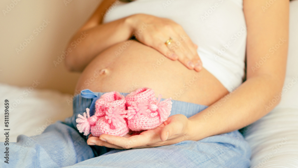 Pregnant woman holding wooden newborn stuff, baby accessories - shoes, toys  on beige background Stock Photo by jchizhe