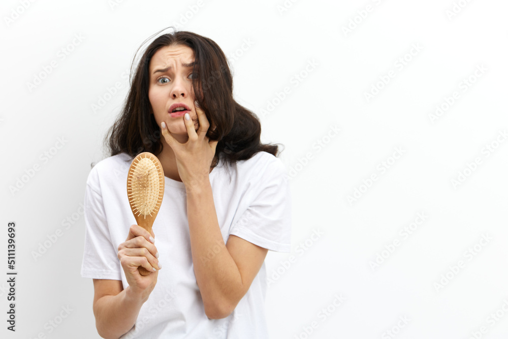 horizontal photo on a white background of a sad, shocked woman holding a wooden comb in her hands and clutching her hair in panic, looking into the camera with her eyes wide open horizontal photo on a white background of a sad, shocked woman holding a wooden comb in her hands and clutching her hair in panic, looking into the camera with her eyes wide open