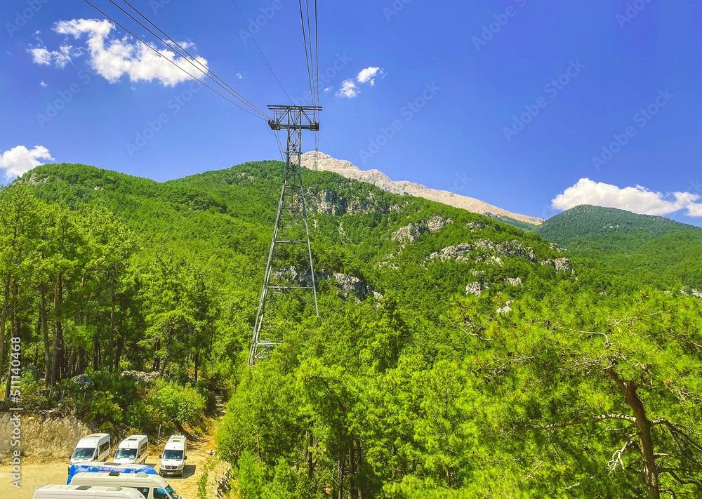 cable car on the mountain. view from a height of green exotic plants and cars. cabin with tourists moves on black, thick cables at a great height