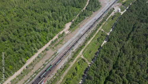Aerial View above close paralel of the Cargo Long Train in taiga, mountains near to dirt road with tracks in sunny summer afternoon photo