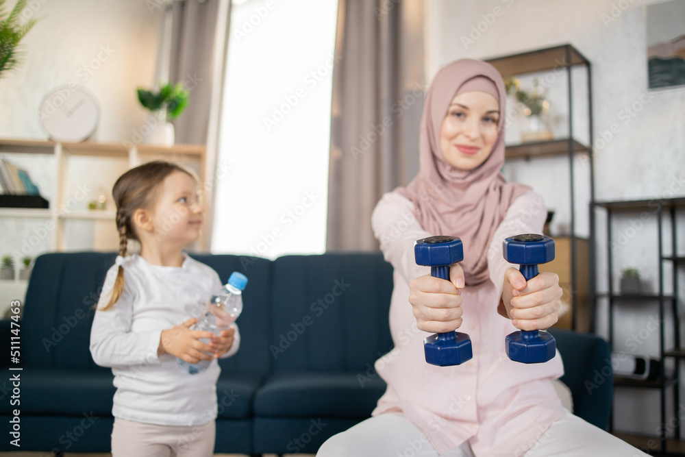 Focus on dumbbells, young Arab family doing sports in a bright living room at the weekend. Happy free time, healthy lifestyle concept. Focus on dumbbells, young Arab family doing sports in a bright living room at the weekend. Happy free time, healthy lifestyle concept.