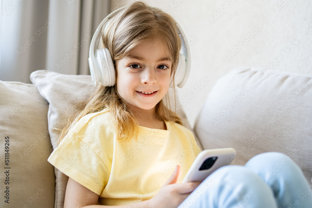 Adorable blonde girl wearing wireless headphones, watching funny video in social network on smartphone or playing online mobile games. Adorable blonde girl wearing wireless headphones, watching funny video in social network on smartphone or playing online mobile games.