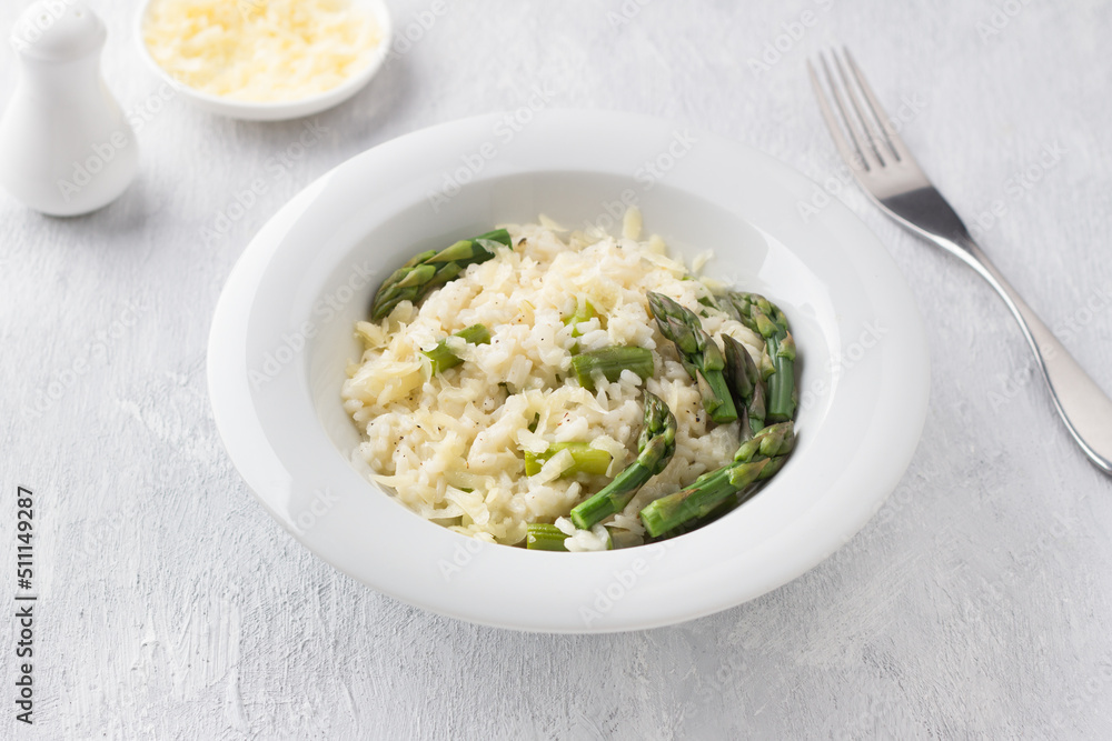 White plate of delicious creamy risotto with asparagus and cheese on a light gray background. traditional italian food