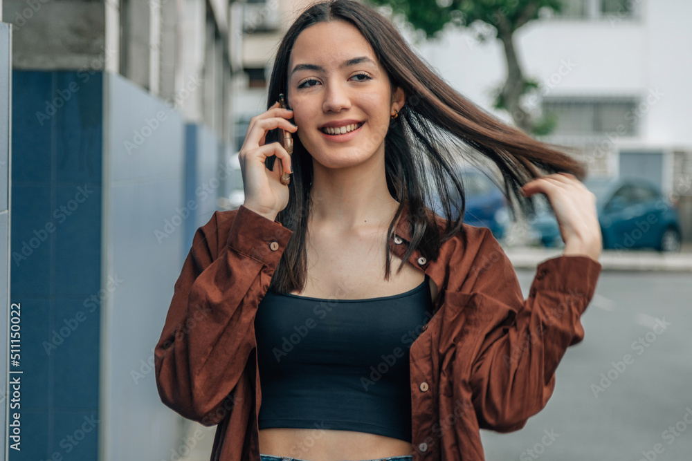 Fototapeta premium smiling young girl talking on mobile phone in the street