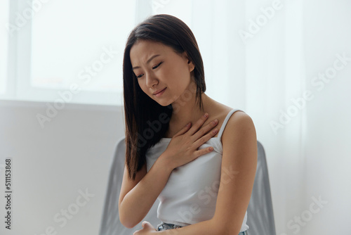 Heart attack. Suffering from pain tanned beautiful young Asian woman hold hand on chest heart crying at home interior living room. Injuries Poor health Illness concept. Cool offer Banner