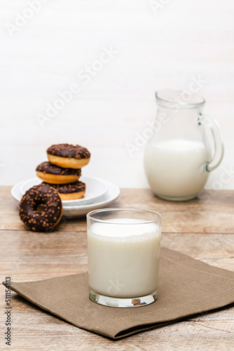 Mini donuts covered with chocolate glaze served with bottle, jug, glass of milk. Stack of tasty sweet sugar creamy or icing doughnuts dessert food on plate and napkin on kitchen. national donuts day