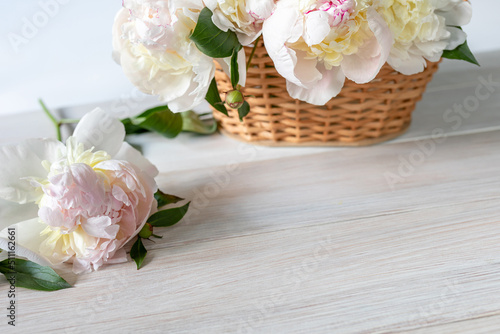 Light peonies in a wicker basket on a white wooden table © LariBat