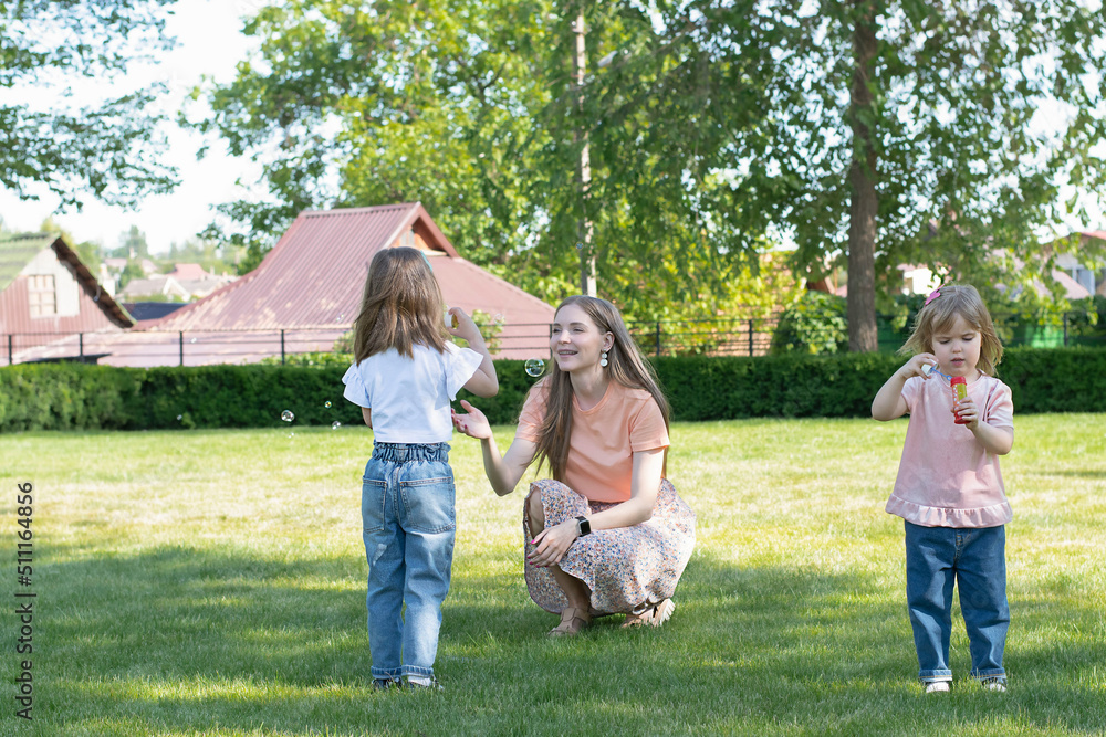 Obraz premium Mom and two daughters have fun playing in the park and blowing soap bubbles.