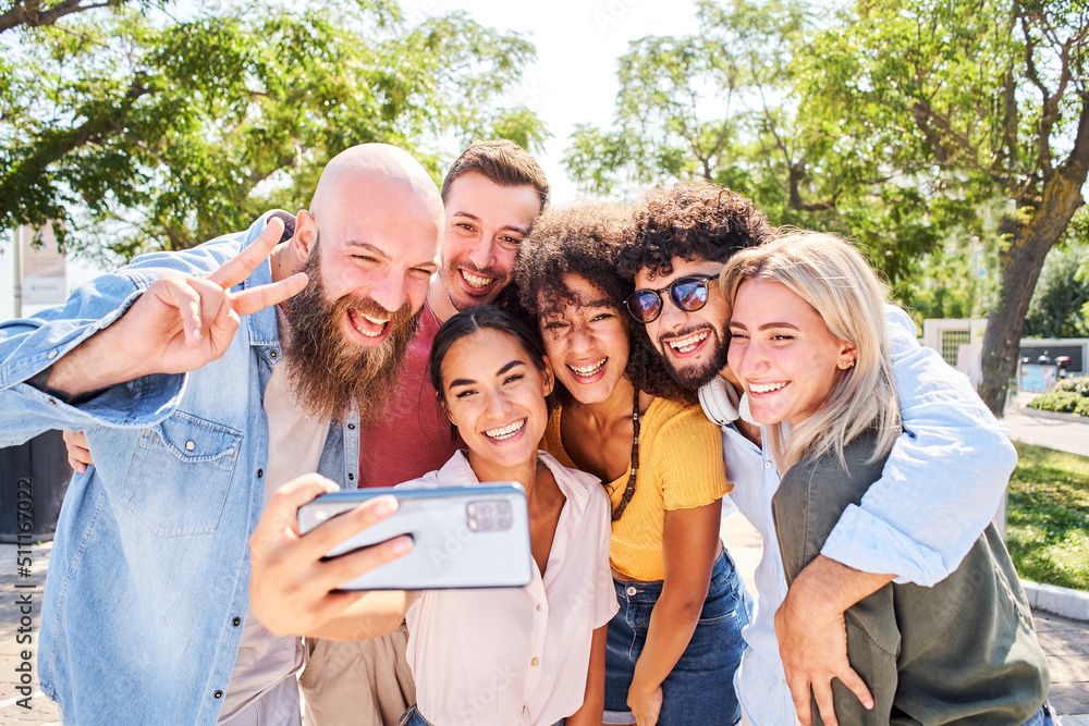 Obraz premium Woman taking mobile phone selfie with a multiracial group of friends. 