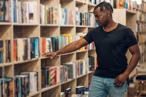African american man picking and reading books in library or bookstore