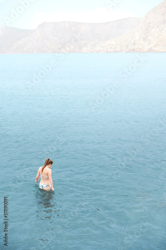 Young adult woman in bikini enters the Mediterranean Sea alone to swim while the water is calm and nobody bothers her. Relax image. Moments of introspection