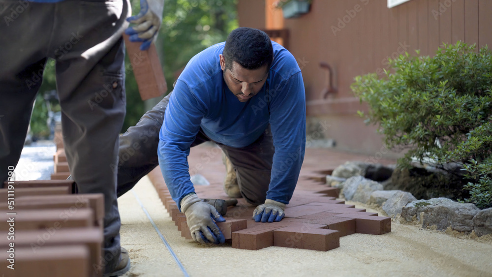 Man putting brick pavers into place in a herringbone pattern in a hardscaping, landscaping patio design. Man putting brick pavers into place in a herringbone pattern in a hardscaping, landscaping patio design.
