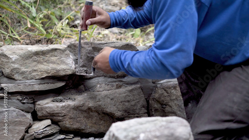 Closeup of putting mortar between large stones in a rock wall design in hardscaping landscaping project.