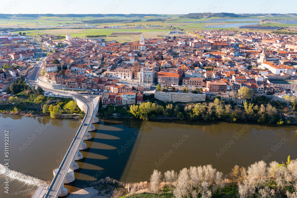 Fototapeta premium Picturesque aerial view of Tordesillas townscape on Duero river overlooking brownish tiled roofs of residential buildings and temples on spring day, Spain
