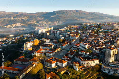 Picturesque drone view of Vila Real cityscape in valley framed by Serra do Alvao and Serras do Marao mountains in light fog on sunny spring day, Portugal