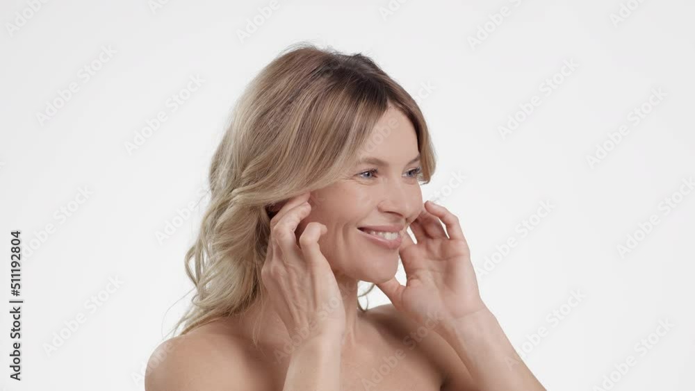 Beautiful mature lady making skin lifting facial massage, semi profile portrait over white background, slow motion Beautiful mature lady making skin lifting facial massage, semi profile portrait over white background, slow motion