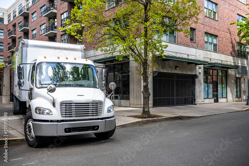 Compact day cab rig semi truck with box trailer making delivery to urban city multilevel apartment neighborhood standing on the street for upload cargo © vit