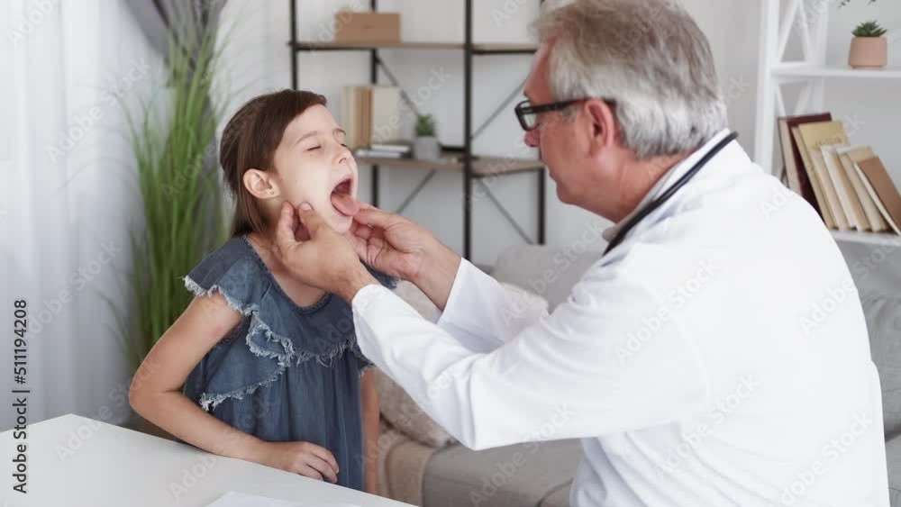 Child healthcare. Pediatrician checkup. Kid flu diagnosis. Middle-aged male doctor examining sick small girl patient sore throat at modern interior. Child healthcare. Pediatrician checkup. Kid flu diagnosis. Middle-aged male doctor examining sick small girl patient sore throat at modern interior.