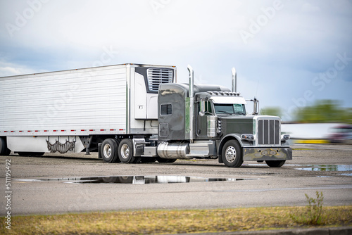 Stylish gray big rig classic semi truck tractor with refrigerator semi trailer standing for the rest on the industrial parking lot waiting for the next load