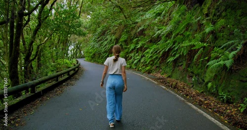 Woman walks along an asphalt road in a dense forest. Overgrown trees in laurel tree forest or jungle, Anaga National Park, Tenerife, Canary Islands, Spain. photo