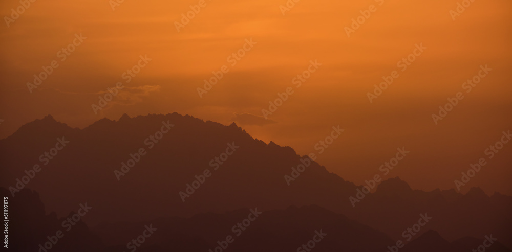 Beautiful evening panoramic landscape with bright setting sun over distant mountain peaks at sunset Beautiful evening panoramic landscape with bright setting sun over distant mountain peaks at sunset