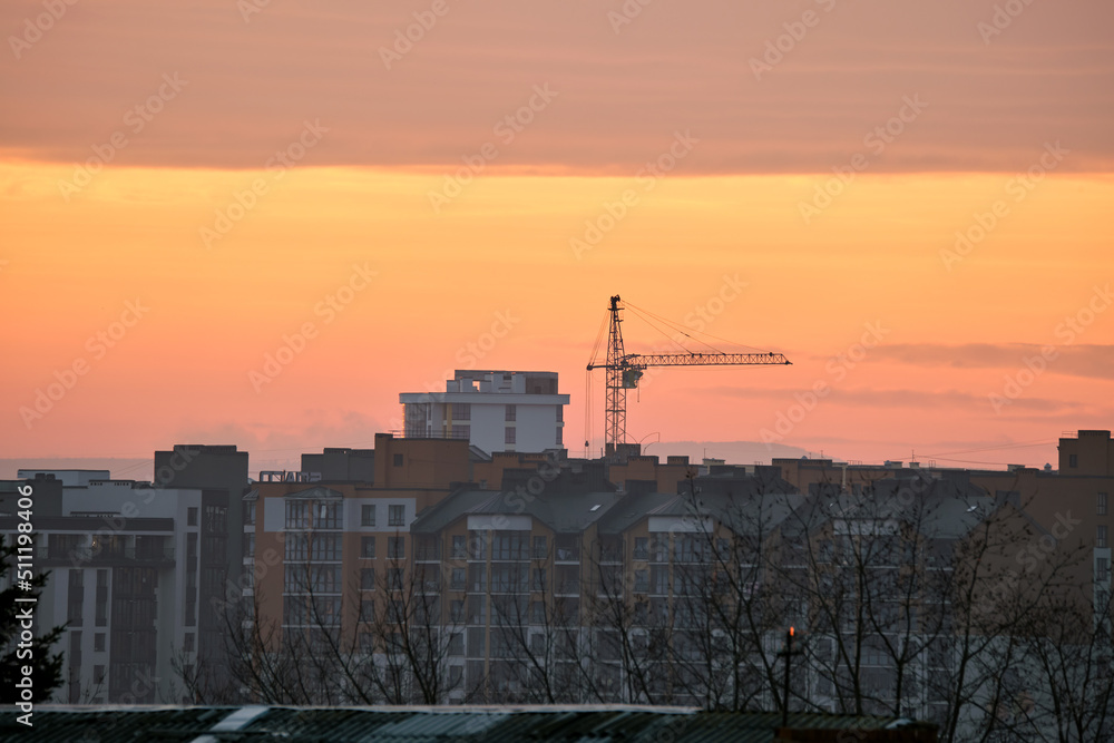 Fototapeta premium Dark silhouette of tower cranes at high residential apartment buildings construction site at sunset. Real estate development