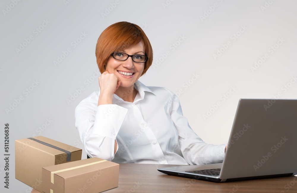 Portrait of businesswoman sitting at table, packing boxes with orders, working on laptop Portrait of businesswoman sitting at table, packing boxes with orders, working on laptop