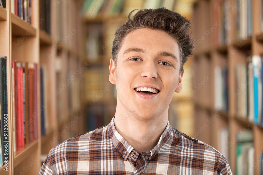 Obraz premium Happy schoolboy guy posing in campus library on bookshelves background.