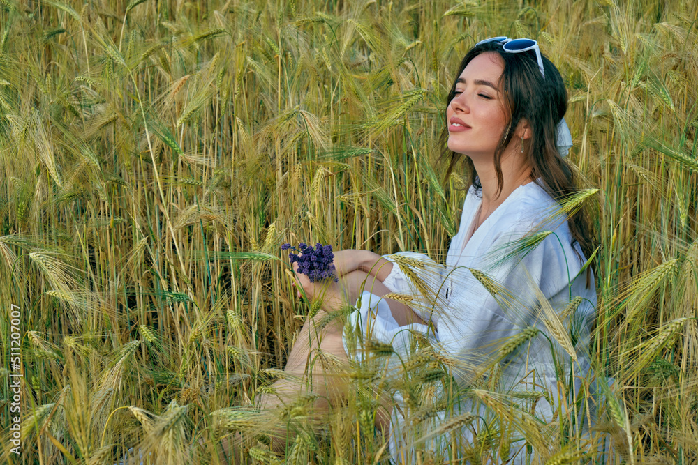 Portrait of a young girl in light clothes sitting in a wheat field