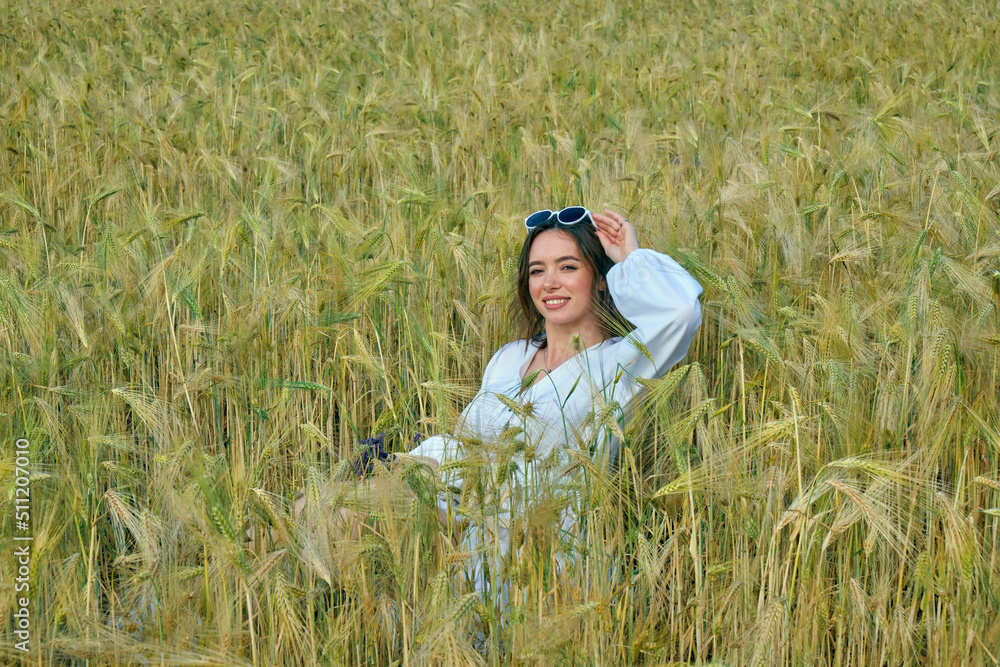 Portrait of a young girl in light clothes sitting in a wheat field