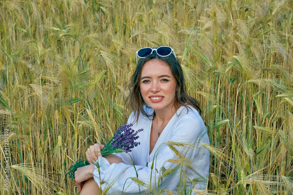 Portrait of a young girl in light clothes sitting in a wheat field
