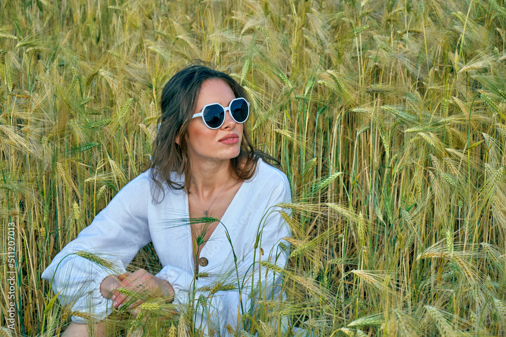 Portrait of a young girl in light clothes sitting in a wheat field