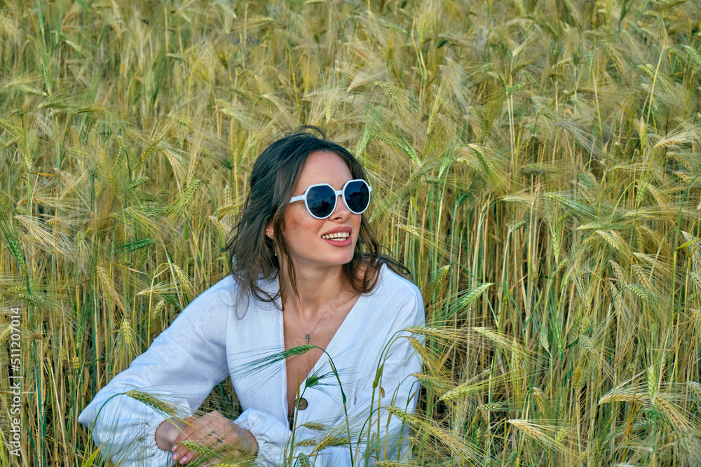 Portrait of a young girl in light clothes sitting in a wheat field